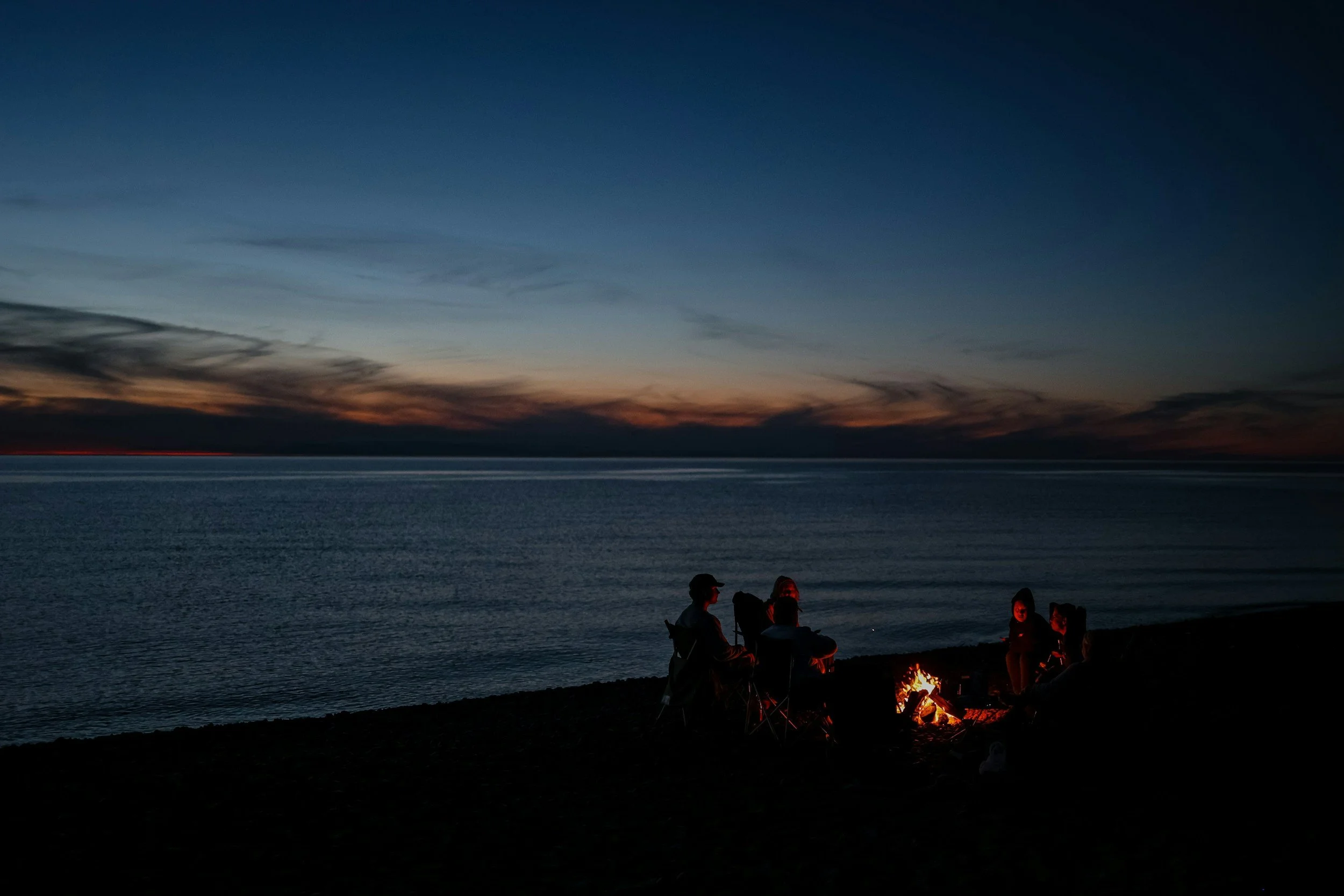 People gathered around a campfire on a beach at dusk