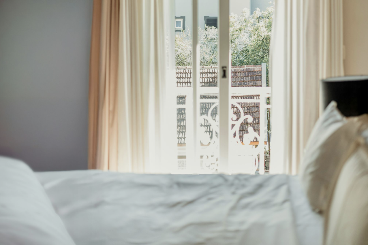 Hotel bed with sunlit balcony doors